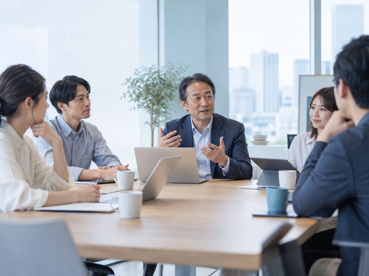 会議で話す経営者と、話を聞く社員